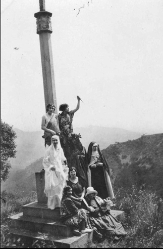 Figura 11. Grup de vuit alumnes, a la creu de l'abat Guimerà de Poblet a Escornalbou, disfressades de personatges literaris. Representats a la fotografia hi ha Beatriu, el Dant, santa Teresa de Jesús, probablement Marguerite Gautier, etc. (1928, AFBD)